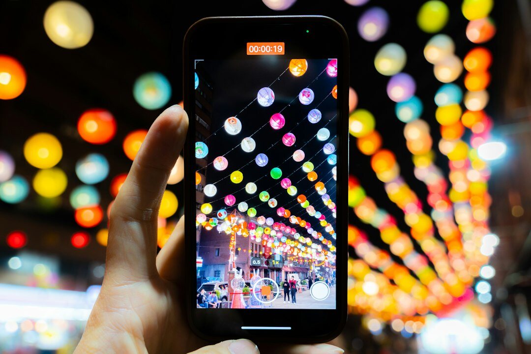 Hand holding a smartphone at night with colorful lights in the background